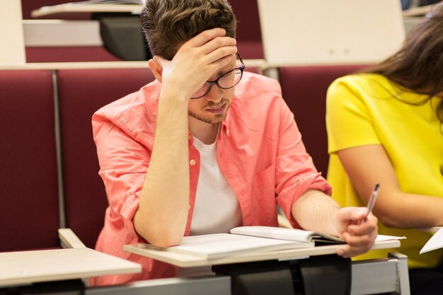 Photo education, high school, university, learning and people concept - group of international students with notebooks writing in lecture hall and talking