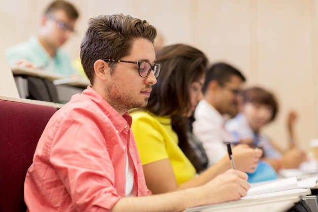 education, high school, university, learning and people concept - group of international students with notebooks writing in lecture hall and talking