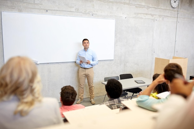 Foto istruzione, scuola superiore, università, insegnamento e concetto di persone - gruppo di studenti internazionali e insegnante con documenti in piedi alla lavagna durante la conferenza