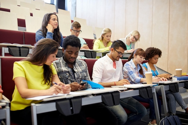 Photo education, high school, university, technology and people concept - group of international students with smartphones and coffee at lecture