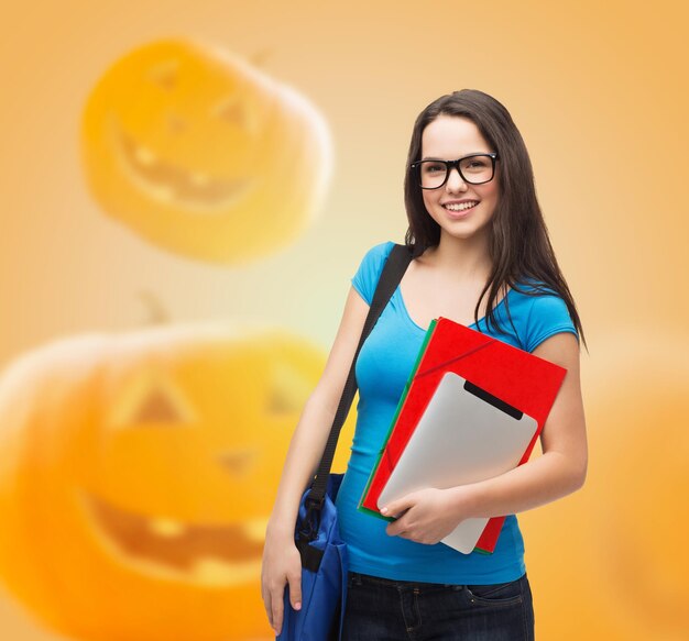 Education, holidays, school and people concept - smiling student girl in glasses with books and bag over halloween pumpkins background