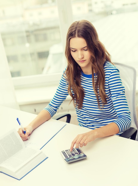 Foto concetto di istruzione e casa - ragazza studentessa concentrata con taccuino, calcolatrice e libro