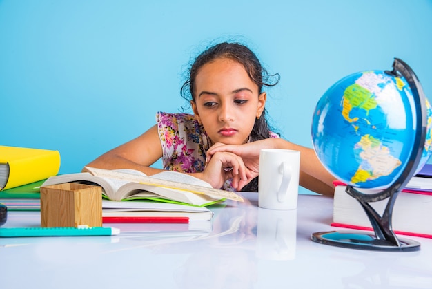 Foto concetto di educazione a casa - piccola ragazza indiana o asiatica carina che studia a casa con una pila di libri, globo educativo ecc. messa a fuoco selettiva