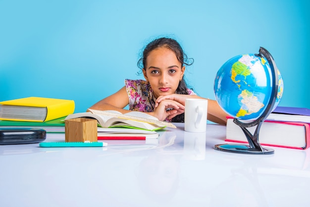 Foto concetto di educazione a casa - piccola ragazza indiana o asiatica carina che studia a casa con una pila di libri, globo educativo ecc. messa a fuoco selettiva