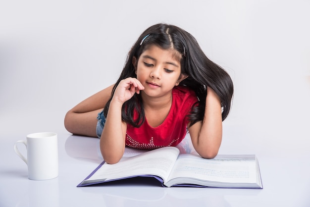 집에서 교육 개념-집에서 바닥에 앉아있는 동안 책과 커피 잔의 더미와 함께 공부하는 귀여운 작은 인도 또는 아시아 소녀. 흰색 배경 위에 절연