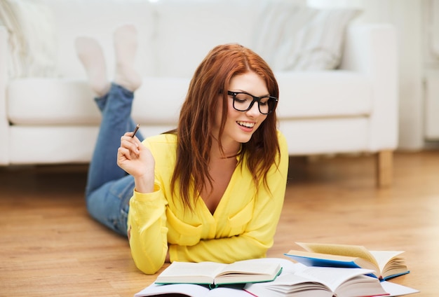 Concetto di educazione e casa - studentessa sorridente con gli occhiali che legge libri a casa