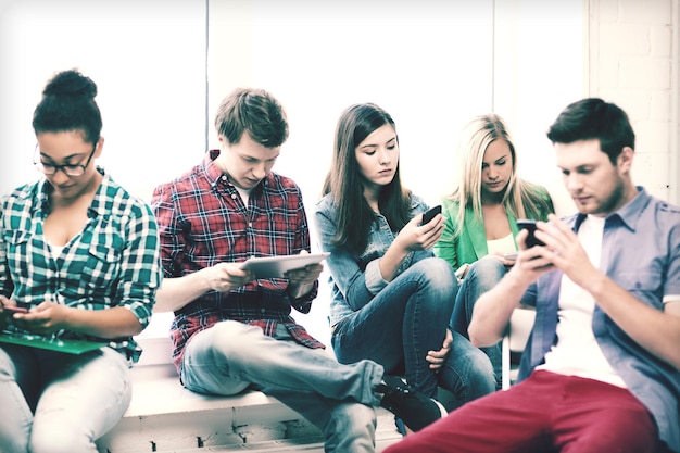 education and internet concept - students looking at their phones and tablet pc at school