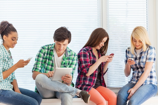 education and internet concept - students looking at their phones and tablet pc at school