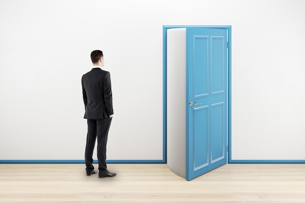 Education and knowledge concept with businessman back view in front of a book that opens as an open door symbolizing knowledge in empty room with white wall and wooden floor