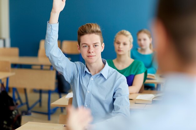 Фото Концепция образования, обучения и людей - счастливый студент поднимает руку на школьном уроке