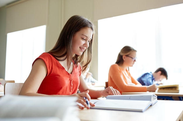 education, learning and people concept - happy student girl with book writing school test