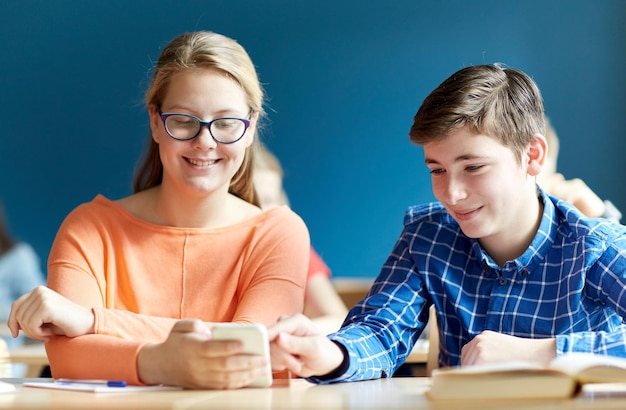 education, learning, technology, communication and people concept - students with smartphone texting at school lesson