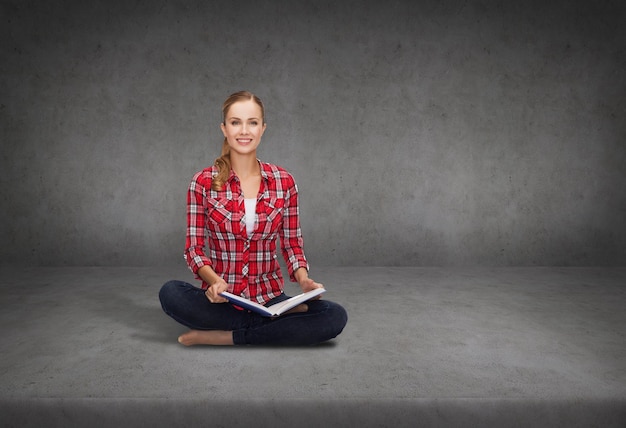 education and leisure concept - smiling young woman sitting on floor with book