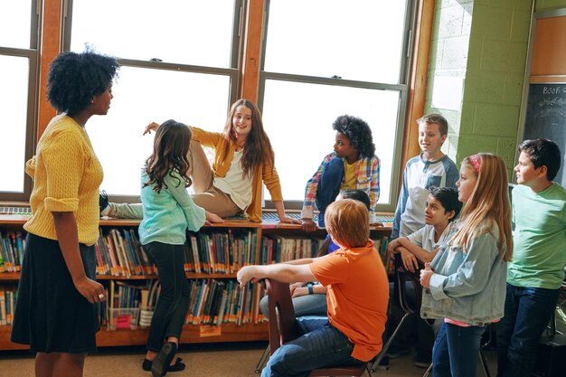 Foto insegnante della biblioteca educativa e studenti dei bambini in classe della scuola elementare borsa di studio per l'apprendimento dello sviluppo e gruppo di bambini che parlano di discussione e studiano per conoscenza con la donna nera