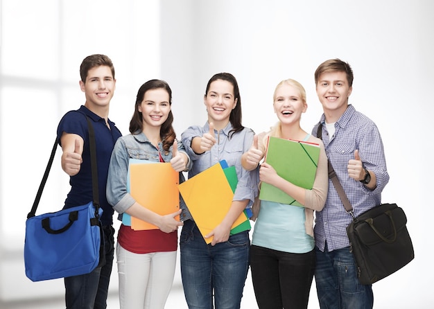 Education and people concept - group of smiling students standing and showing thumbs up