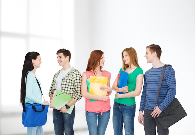 education and people concept - group of smiling students with bags and folders having discussion