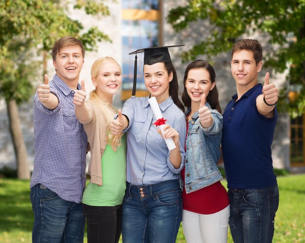 education and people concept - group of standing smiling students with diploma and corner-cap showing thumbs up