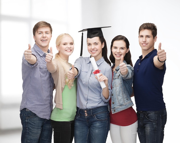 education and people concept - group of standing smiling students with diploma and corner-cap showing thumbs up