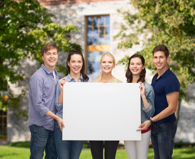 education and people concept - group of standing smiling students with white blank board