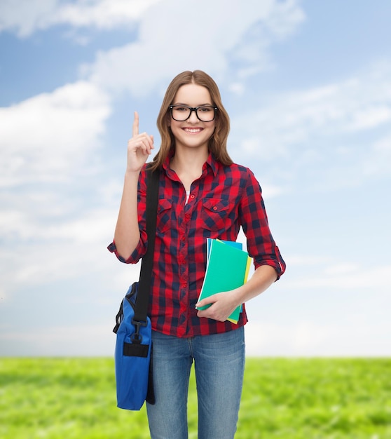 education and people concept - smiling female student in eyeglasses with bag and notebooks showing direction