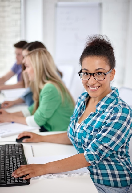 education, people, friendship, technology and learning concept - group of happy international high school students or classmates in computer class