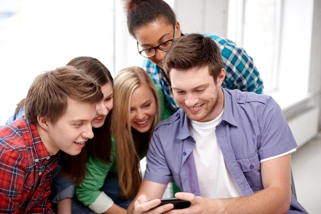 education, people, friendship, technology and learning concept - group of happy international high school students or classmates with smartphone in classroom