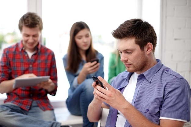 education, people, friendship, technology and learning concept - group of high school students or classmates with smartphone in classroom