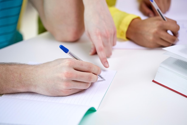 education, people and school concept - close up of students hands with notebooks writing at school