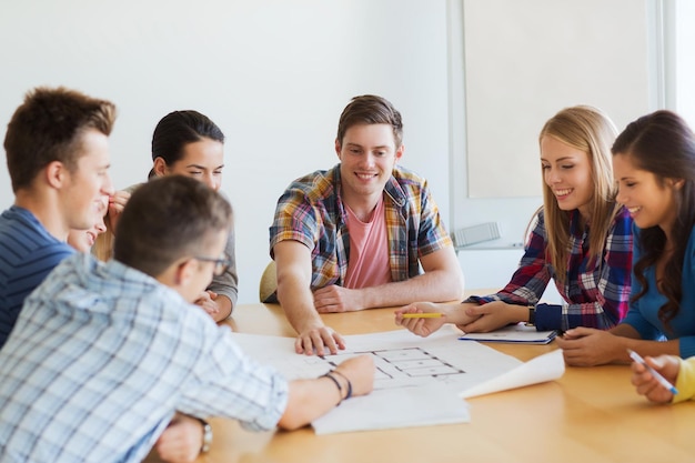 education, school, architecture and people concept - group of smiling students with blueprint meeting indoors