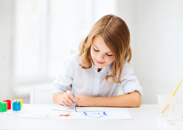 education, school, art and painitng concept - little student girl painting at school