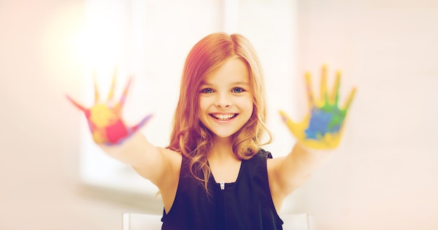 education, school, art and painitng concept - little student girl showing painted hands at school