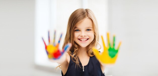 教育、学校、芸術、痛みを伴う概念-学校で塗られた手を見せている笑顔の小さな学生の女の子