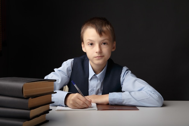 Education at school concept. Boy sitting at the table and studying isolated in the grey classroom.