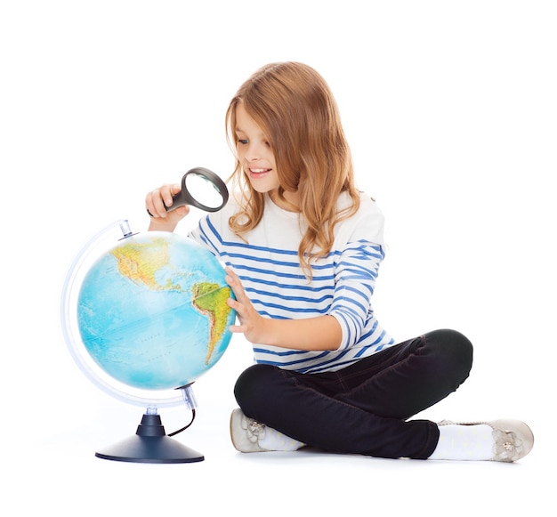 education and school concept - little student girl looking at globe with magnifier