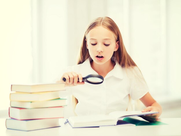 教育と学校の概念-学校で拡大鏡で本を読んでいる小さな学生の女の子