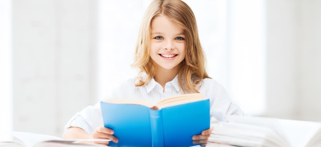 education and school concept - little student girl studying and reading book at school