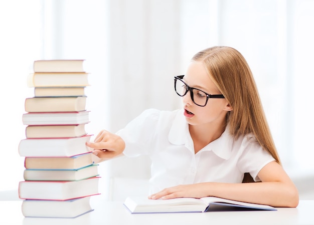 education and school concept - little student girl studying and reading books at school