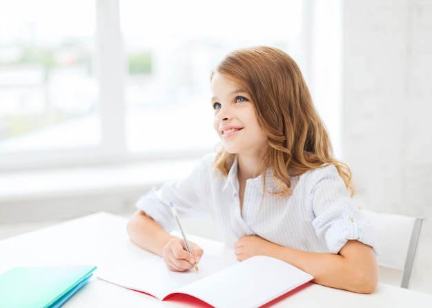 education and school concept - little student girl writing in notebook at school