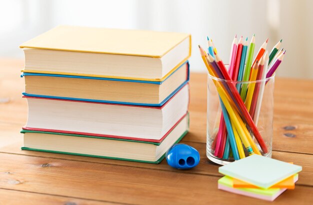 education, school, creativity and object concept - close up of crayons or color pencils with books, stickers and sharpener on wooden table