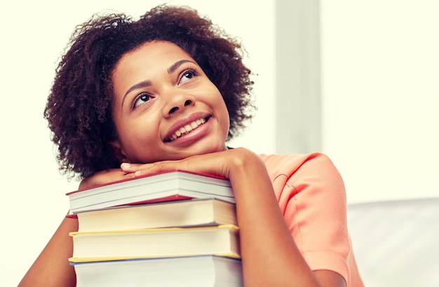 education, school, knowledge and people concept - happy smiling african american student girl with books sitting at table and dreaming at home