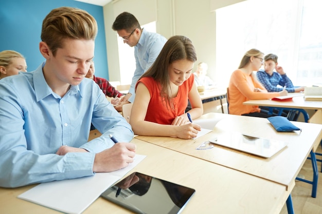 教育、学校、学習、教育、人々のコンセプト – 教室でテストや試験を書く学生と教師のグループ