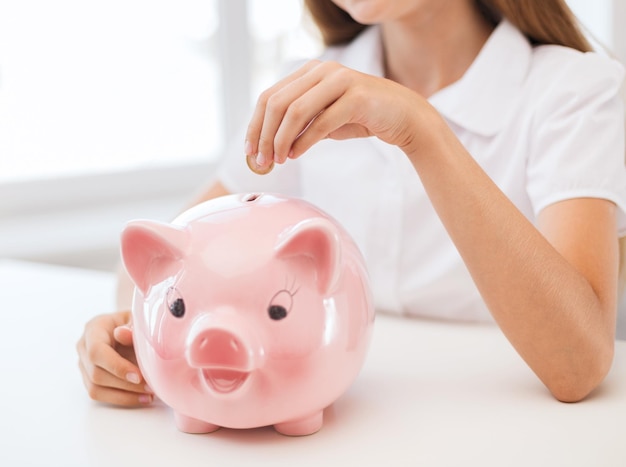 education, school and money saving concept - smiling child putting coin into big piggy bank