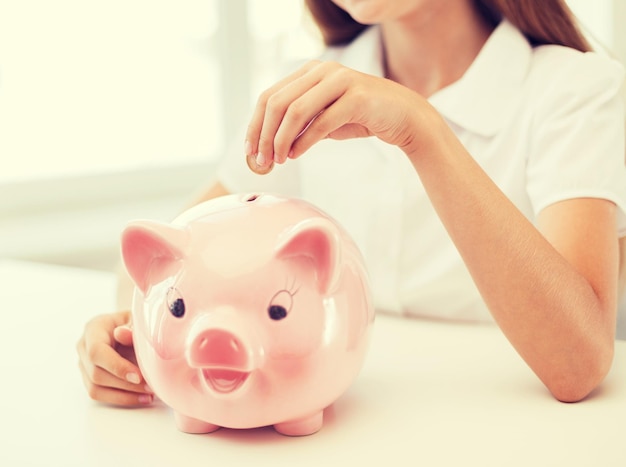 education, school and money saving concept - smiling child putting coin into big piggy bank