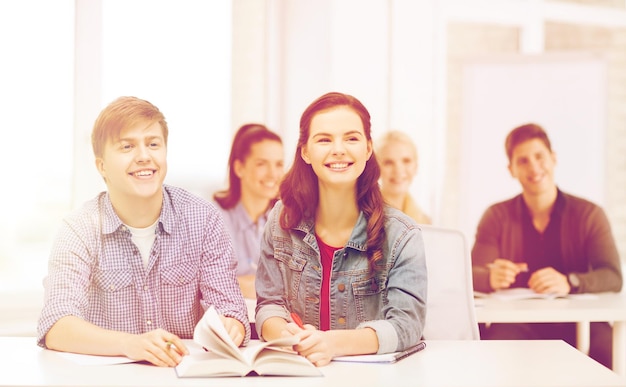 education, school and people concept - two teenagers with notebooks amd book listening to someone at school