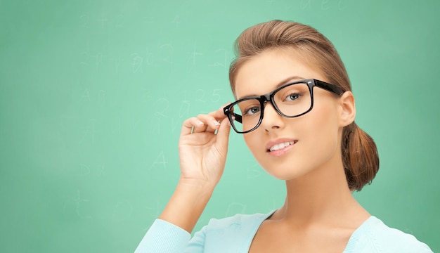 education, school, people and vision concept - happy teenage student girl or woman in eyeglasses over green school chalk board background