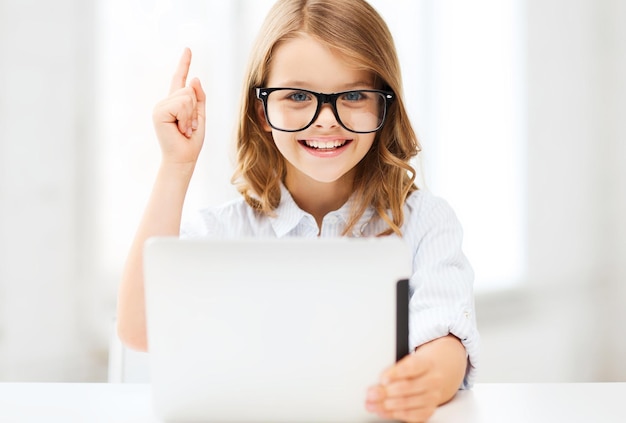 Education, school, technology and internet concept - little\
student girl in black eyeglasses with tablet pc computer and finger\
up at school