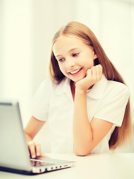 education, school, technology and internet concept - little student girl with laptop pc at school