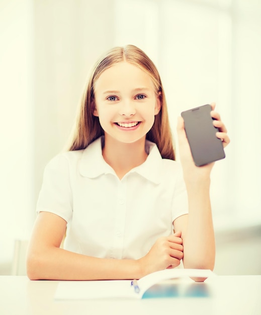 концепция образования, школы, технологий и интернета - маленькая ученица со смартфоном в школе
