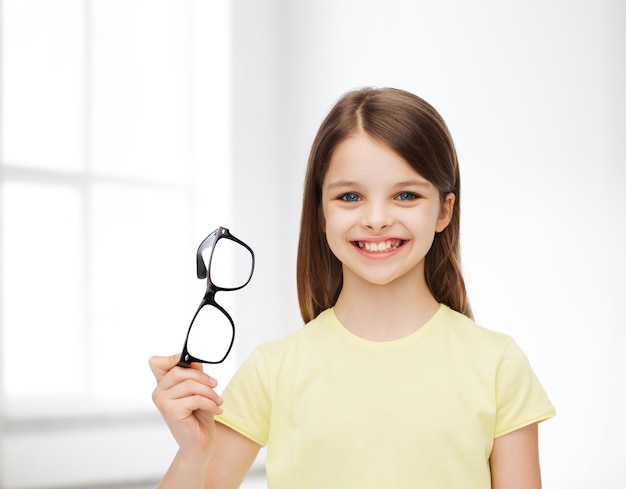 education, school and vision concept - smiling cute little girl holding black eyeglasses