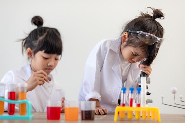 Education, science, chemistry and children concept - kids or students with test tube making experiment at school laboratory